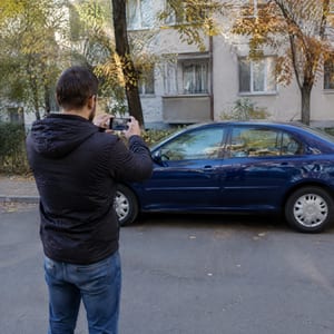 Un bărbat își fotografiază cu telefonul mașina parcată, ca s-o pună la vânzare