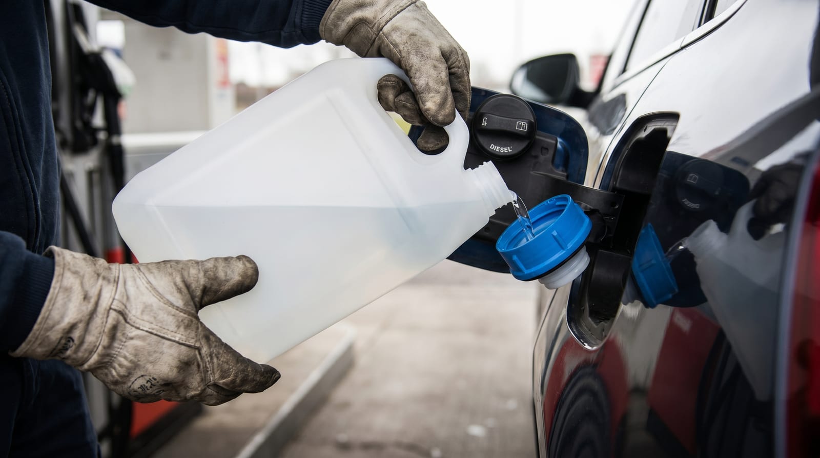 Mâini care toarnă AdBlue dintr-o canistră în rezervorul cu capac albastru al unei mașini diesel