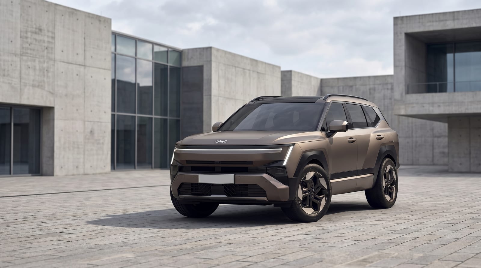 Noul Hyundai Tucson în nuanță bronz, cu siluetă colțuroasă și bandă luminoasă LED pe toată lățimea, parcat pe o piațetă pavată lângă clădiri de beton