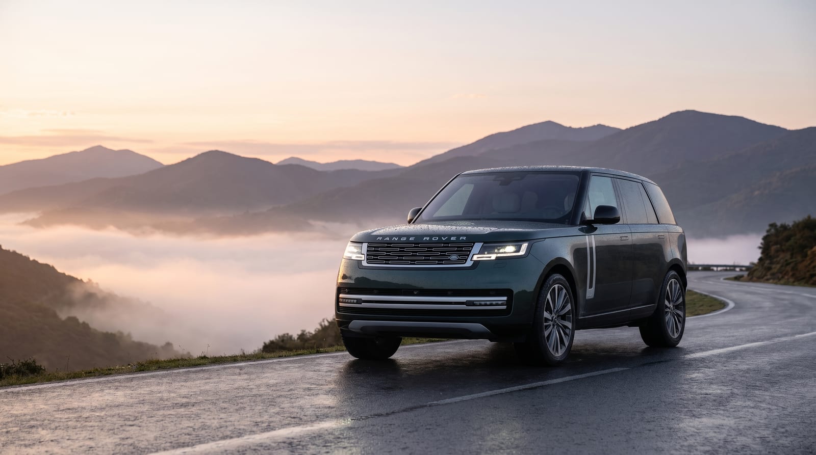 Range Rover Electric verde închis, în trei sferturi față, pe un drum de munte umed, cu ceață în vale la răsărit
