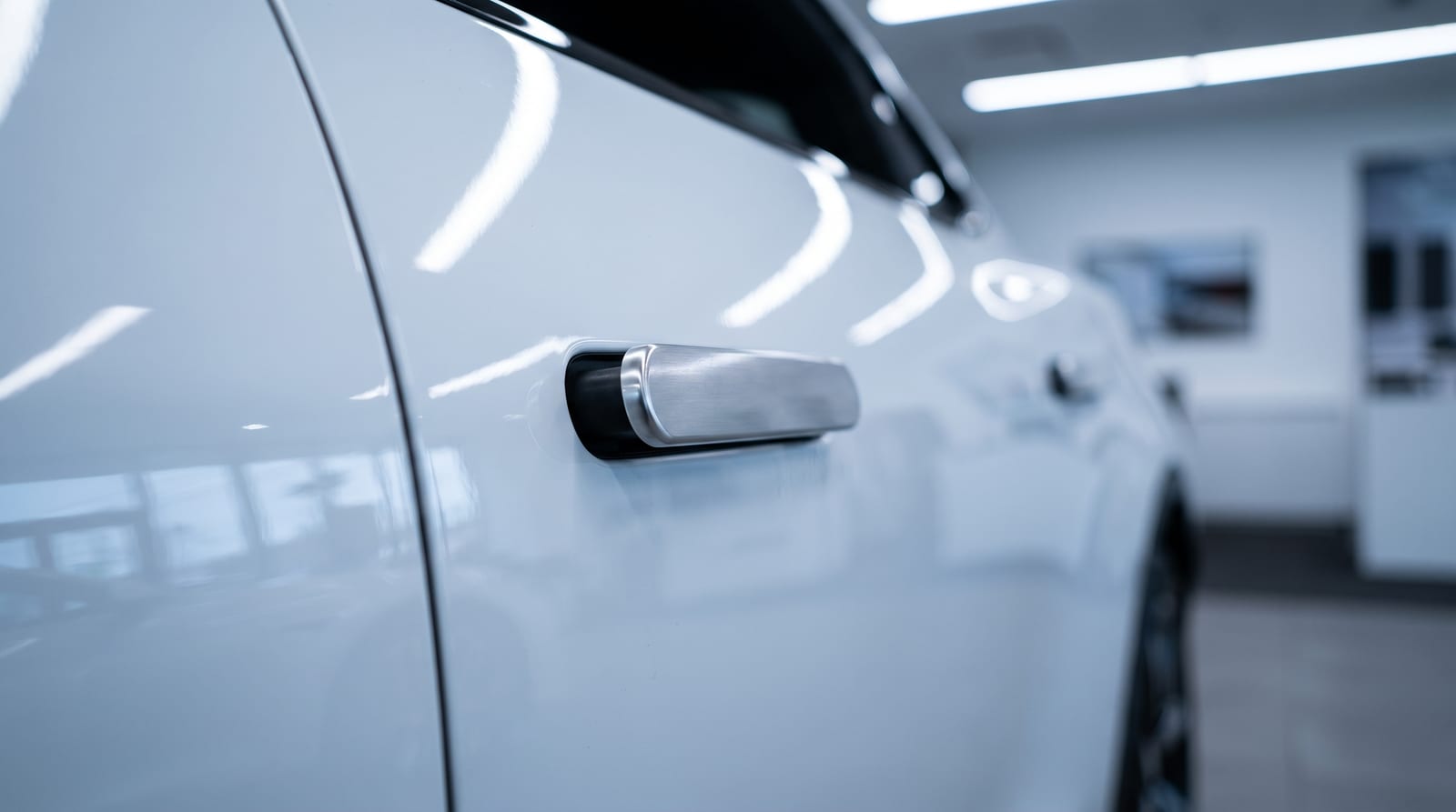 Mâner de ușă retractabil ieșit din portiera unei mașini electrice albe, cu reflexii reci de showroom pe caroserie