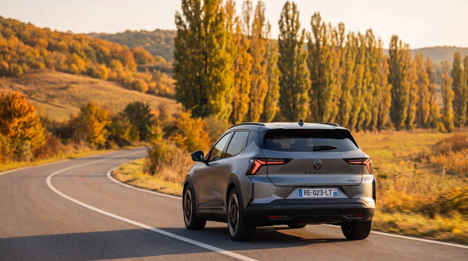 SUV electric Renault Scenic E-Tech gri, în trei sferturi spate, pe un drum de deal, într-o zi de toamnă