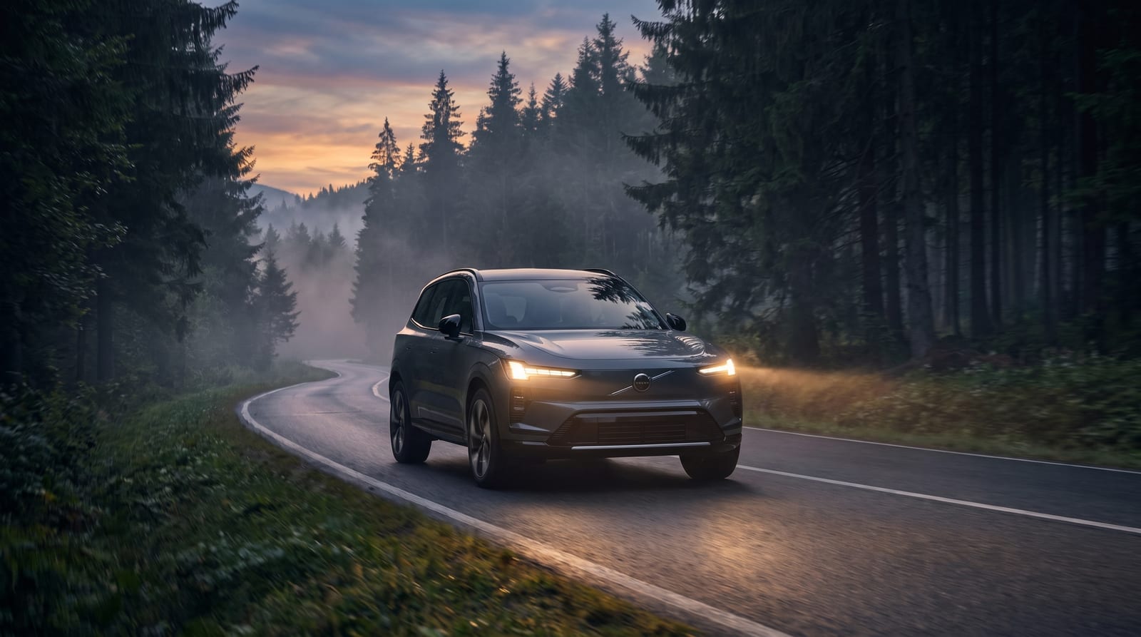SUV electric Volvo rulând cu farurile aprinse pe un drum de pădure în amurg, cu ceață joasă printre brazi